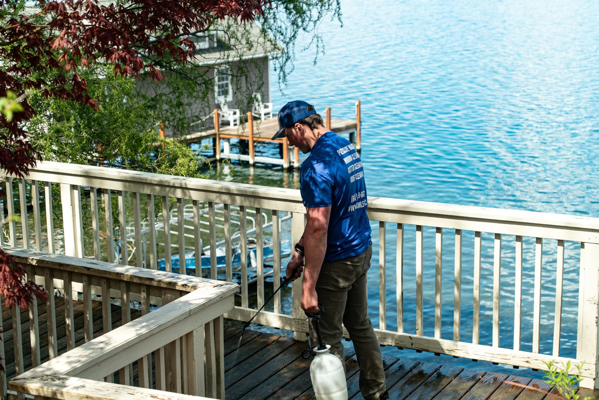 Six Mile crew member treating a lakefront deck overlooking the water in Cazenovia