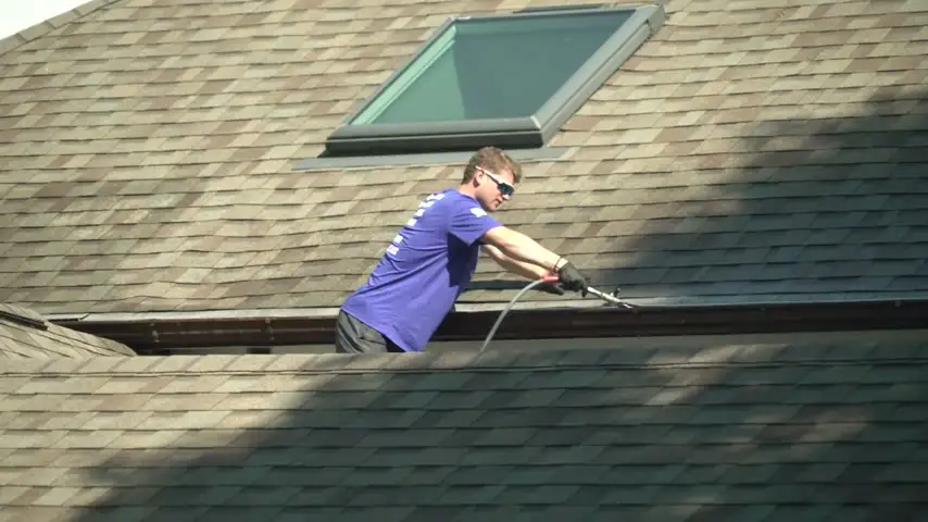 Six Mile crew member working along a roofline clearing a gutter