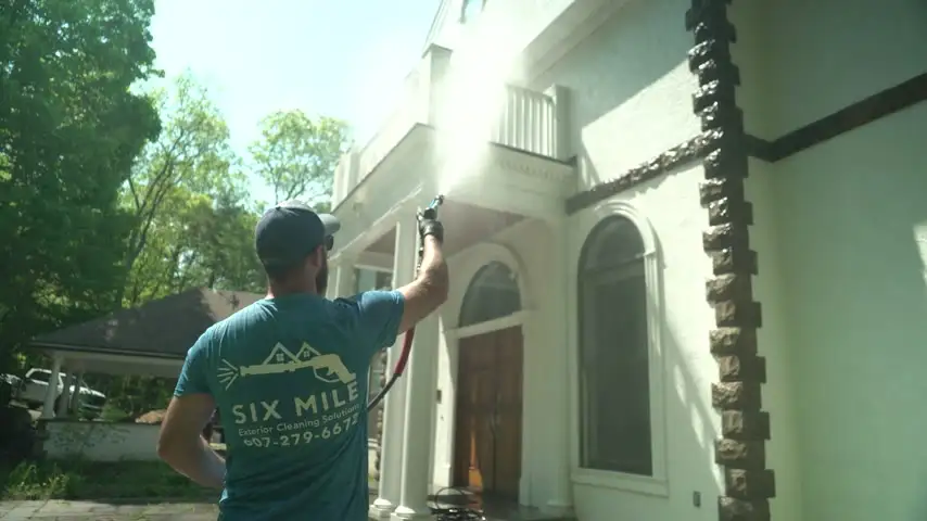 Six Mile technician soft washing the siding of a large home in sunlight
