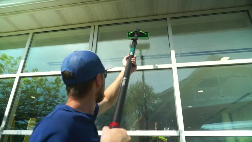 Six Mile crew member pure-water cleaning a tall window with an extension pole