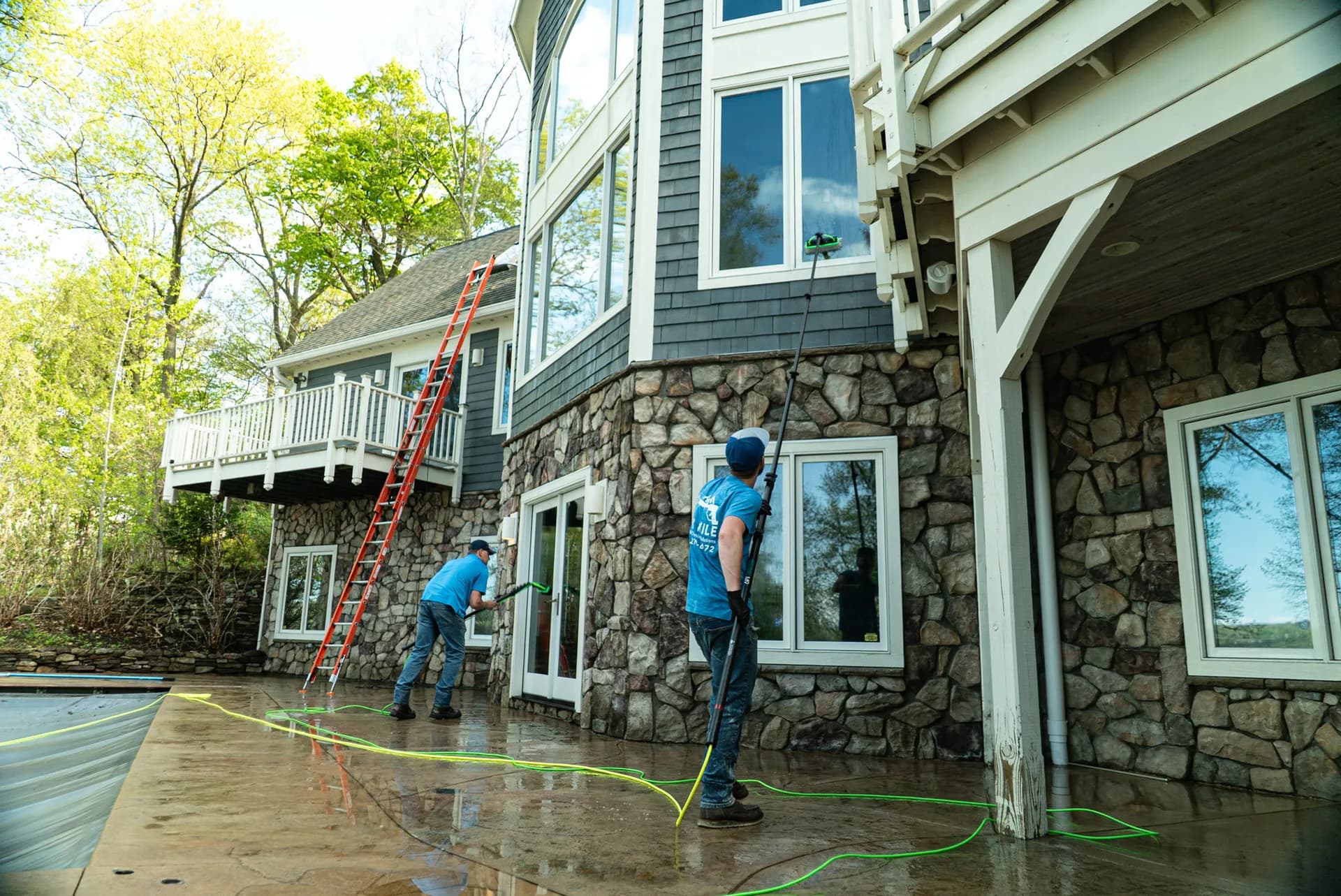 Six Mile crew members pure-water window cleaning a stone and shingle home